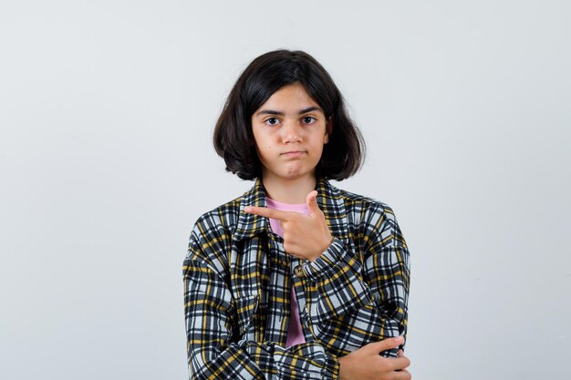 Preteen girl in shirt,jacket pointing aside , front view.