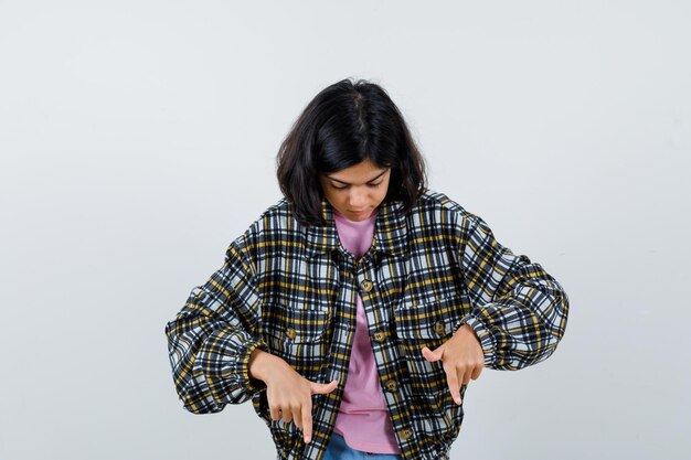 Preteen girl in shirt,jacket pointing down , front view.