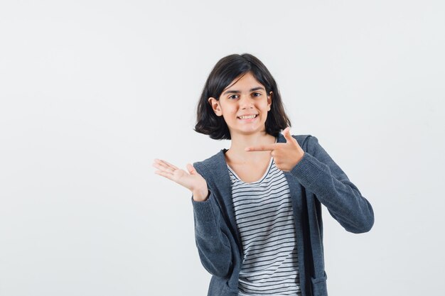 Preteen girl in shirt,jacket pointing at her hand and looking glad ,