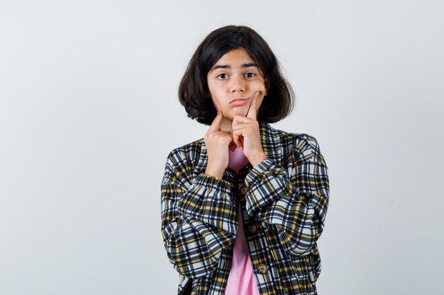 Preteen girl in shirt,jacket squeezing her cheeks , front view.