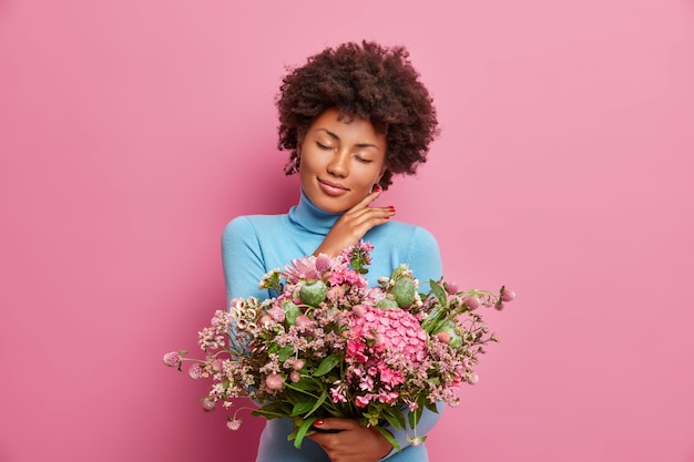 Free photo pretty affectionate woman touches gently jawline stands with closed eyes holds big bunch of flowers