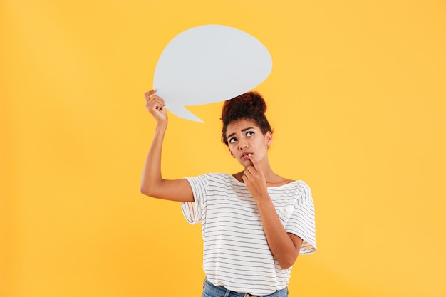 Pretty african lady holding blank speech bubble while standing isolated