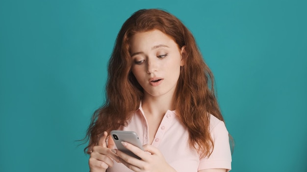 Pretty astonished redhead girl using smartphone on camera over colorful background Amazed expression