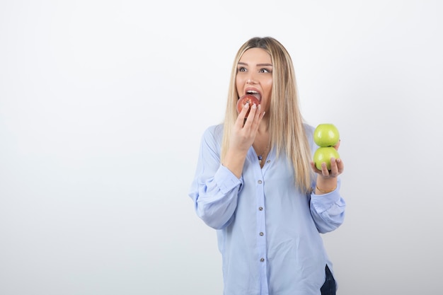 赤い新鮮なリンゴを立って食べているかなり魅力的な女性モデル。