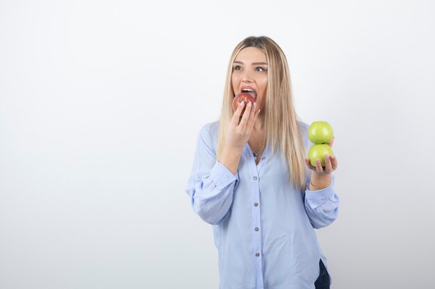 довольно привлекательная модель женщины стоя и ест красное свежее яблоко.