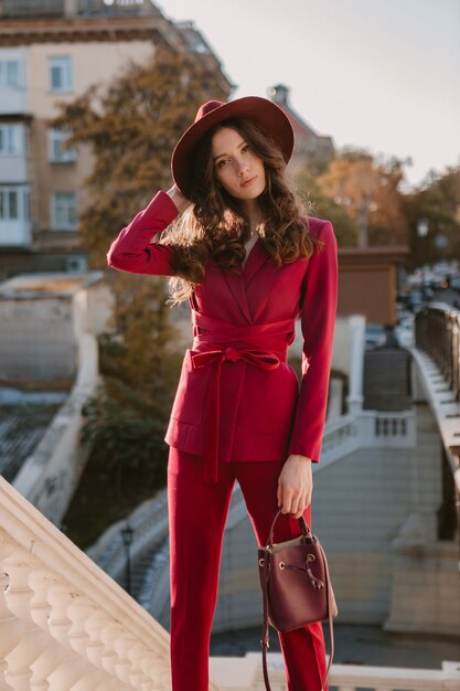 Pretty beautiful stylish woman in purple suit walking in city street, spring summer autumn season fashion trend wearing hat, holding purse