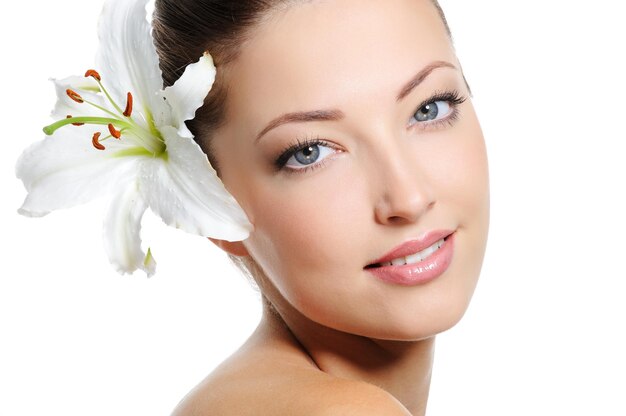 Pretty beautiful woman face with health skin and white lily in her hairs
