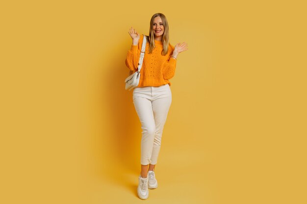 Pretty  blond woman in  trendy autumn outfit  posing on yellow. Holding white leather bag. Full lenght.