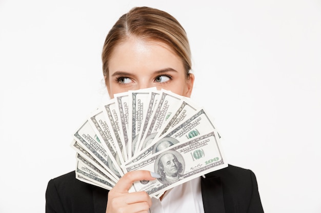 Pretty blonde business woman hiding behing the money and looking away over white wall