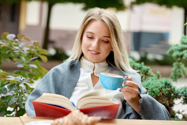 Довольно блондинка читает книгу, сидя в кафе на открытом воздухе в гостиной