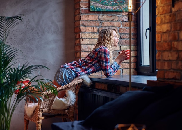 Foto gratuita la femmina abbastanza bionda dei pantaloni a vita bassa beve il caffè del mattino in un bagno con interni soppalcati.