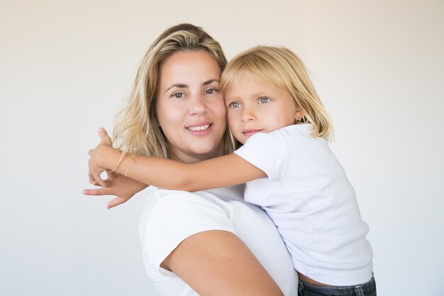 Pretty blonde mother holding daughter and looking at camera