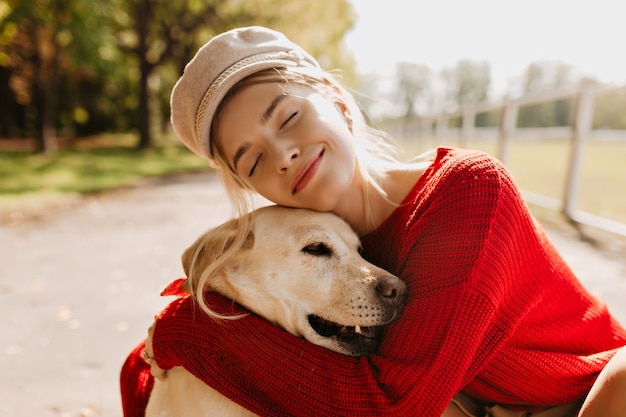 Pretty blonde with her beloved dog spending time together outdoor in the autumn. Nice portrait of a beautiful woman and her pet in the park.