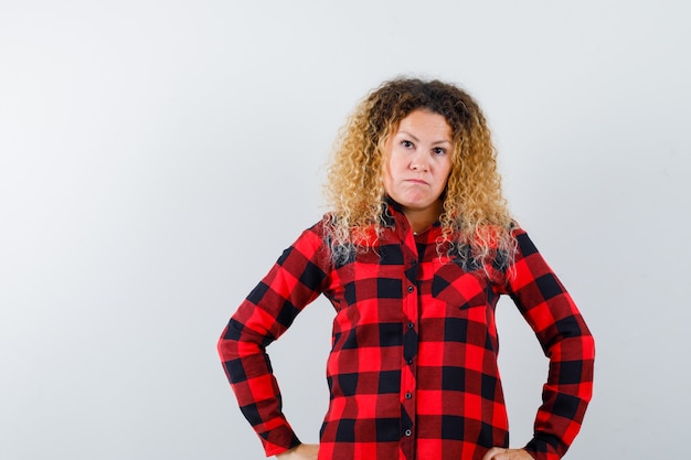 Free photo pretty blonde woman in checked shirt keeping hands on hips and looking serious , front view.