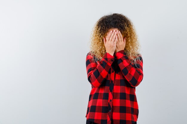 Pretty blonde woman covering face with hands in checked shirt and looking depressed. front view.