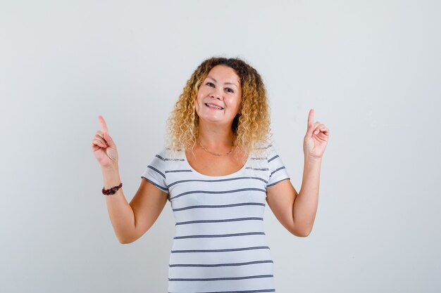 Pretty blonde woman pointing up in striped t-shirt and looking optimistic , front view.