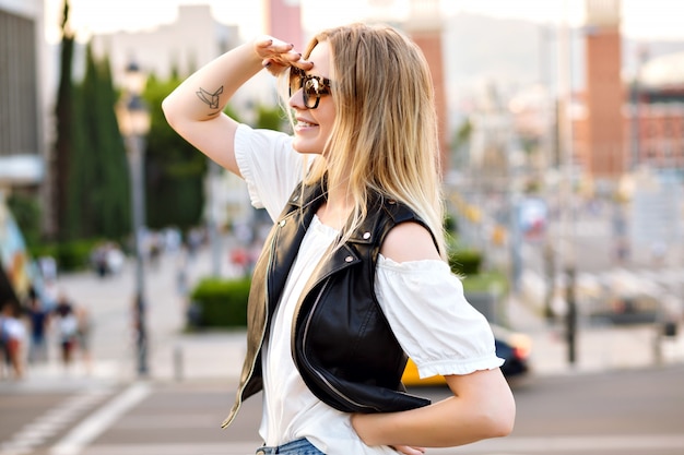 Довольно блондинка позирует на красивой европейской улице, в повседневной одежде и солнцезащитных очках