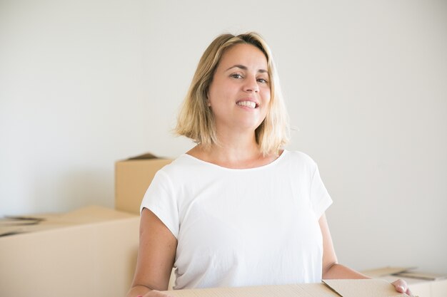 Pretty blonde woman standing with box in new house or apartment