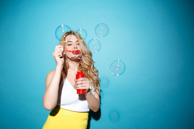 Pretty blonde woman in summer clothes blowing soap bubbles