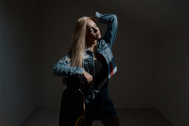 Pretty blonde woman with longboard in dark room