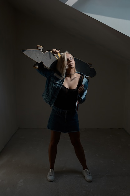 Pretty blonde woman with longboard in dark room