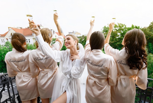 Pretty bride enjoying wedding morning with bridesmaids and holdiing glasses