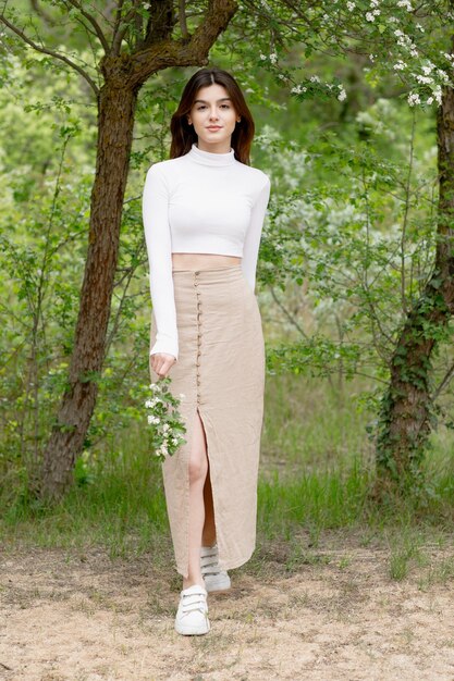 Pretty brunette female standing looking at camera smiling holding blooming branch