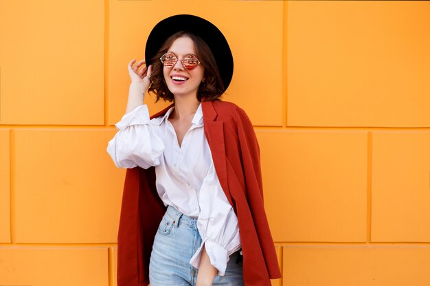 Pretty brunette girl in stylish hat posing over yellow wall.