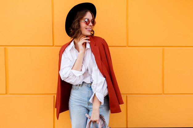 Pretty brunette girl in stylish hat posing over yellow wall.