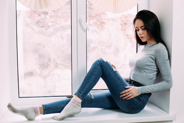 Free photo pretty brunette sits on white windowsill