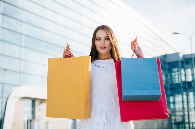 Pretty brunette with long hair stands with shopping bags before a modern glass building