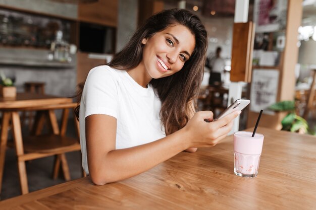 Симпатичная брюнетка с телефоном в руках отдыхает в кафе