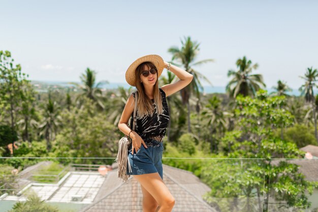 Pretty brunette woman in straw hat enjoying sightseeing, tropical landscape from resort