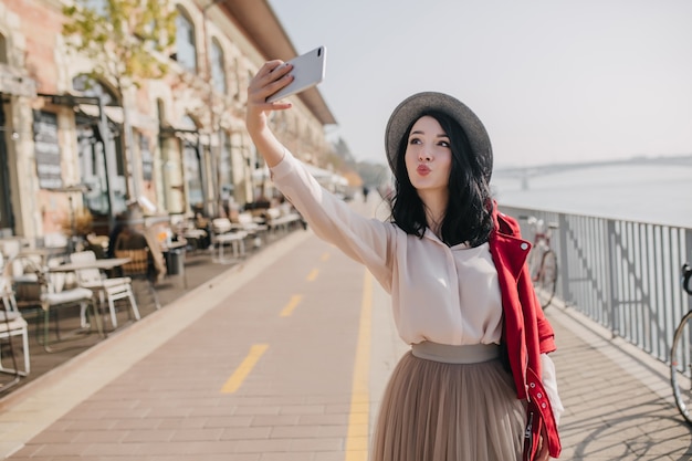 Pretty brunette woman wears elegant blouse and skirt making selfie with kissing face expression