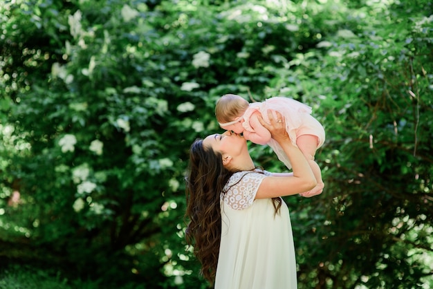 Pretty brunette woman in white dress poses with her little daughter in the garden