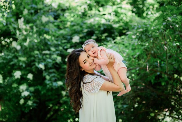 Pretty brunette woman in white dress poses with her little daughter in the garden