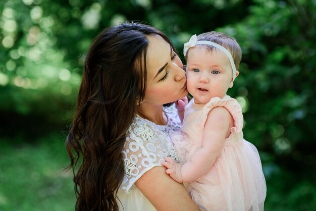 Pretty brunette woman in white dress poses with her little daughter in the garden