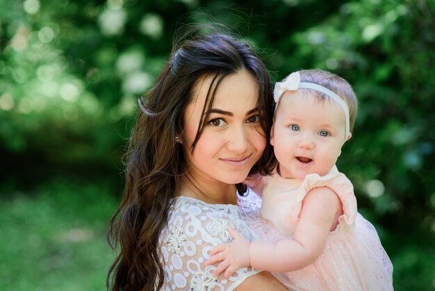 Pretty brunette woman in white dress poses with her little daughter in the garden