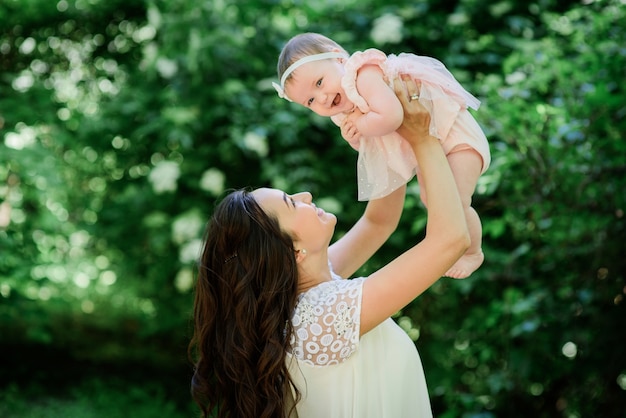 Pretty brunette woman in white dress poses with her little daughter in the garden