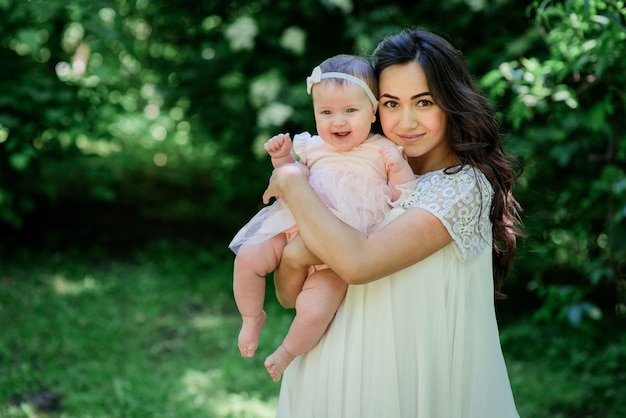 Pretty brunette woman in white dress poses with her little daughter in the garden