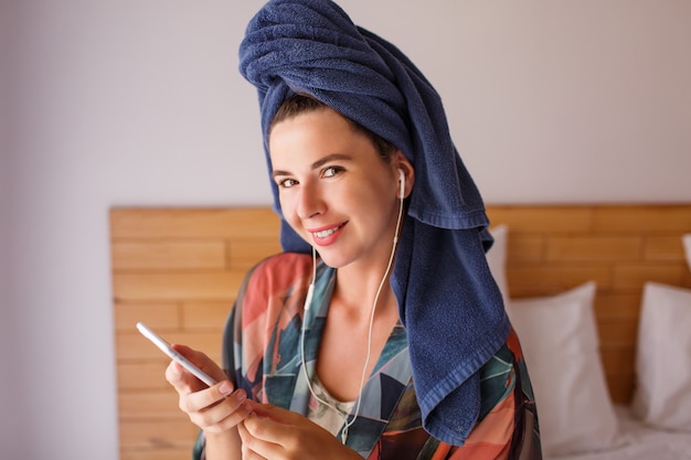 ベッドの上に座っている間携帯電話を使用してシャワータオルに包まれたかなりブルネットの女性