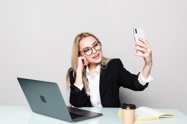 Милая бизнес-леди в офисе держа ее мобильный телефон одной рукой и делая видео звонок на офисном столе