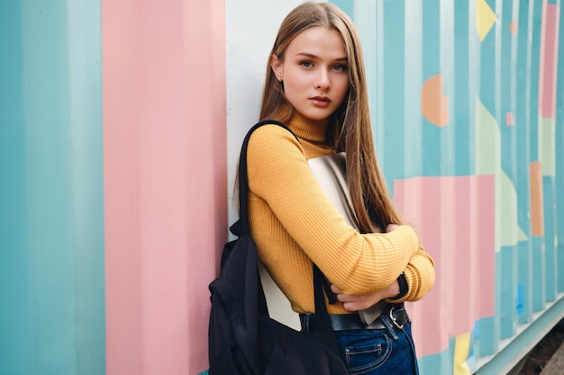 Pretty casual student girl with laptop intently looking in camera over colorful background outdoor