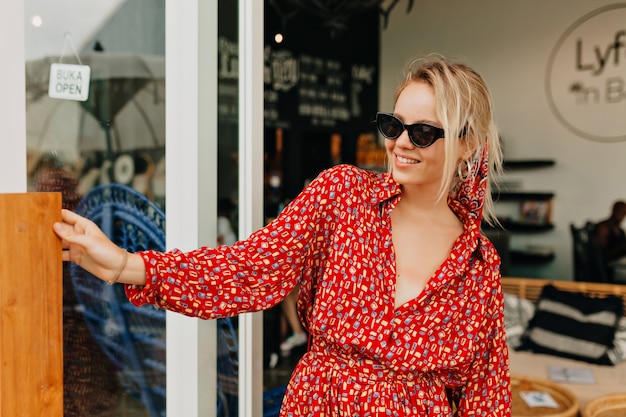 Pretty charming lady in summer bright dress and sunglasses going out from stylish cafeteria