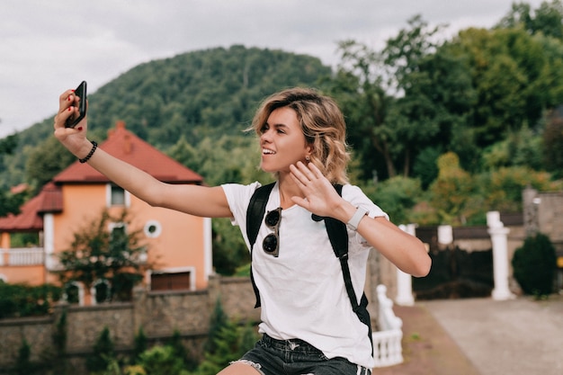 晴れた良い日に山を越えてスマートフォンで自分撮りを作るかなり魅力的な旅行者の女性。旅行のコンセプト、休暇、旅行