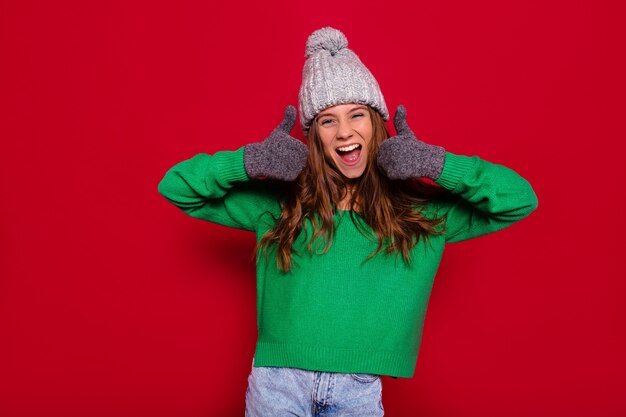 Pretty charming young woman on red wall in winter outfit