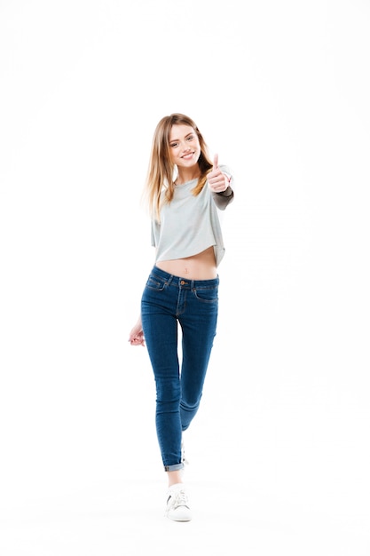 Pretty cheerful young woman standing and showing thumbs up gesture