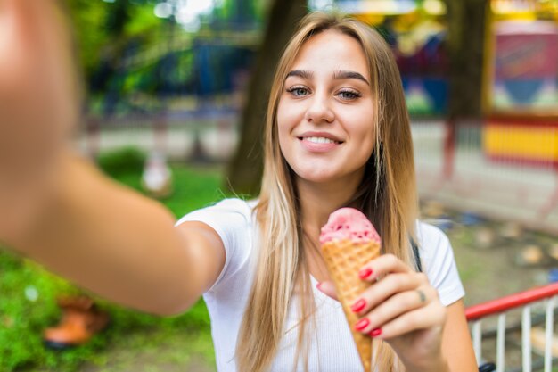 Pretty cheerful young woman walking in park with ice cream