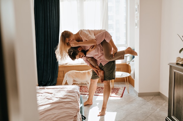 Pretty curly girl jumped on boyfriends back.Love story of couple capering in cozy spacious room.