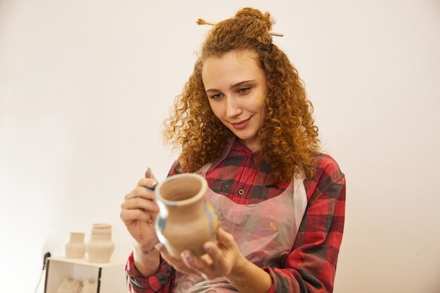Pretty curly girl paints a vase before baking